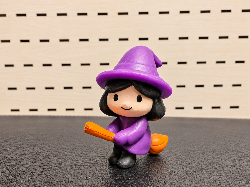 Figura decorativa de brujita morada con escoba naranja