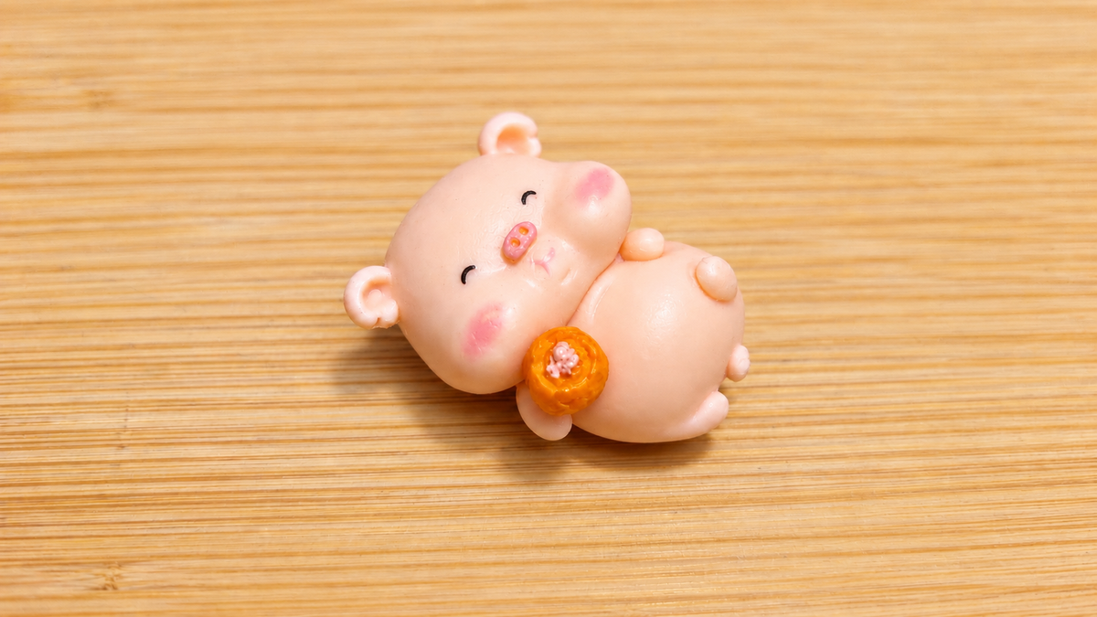 Figura cerdito tumbado con un caramelo naranja