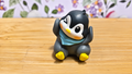 Figura de pingüino sentado con bufanda azul